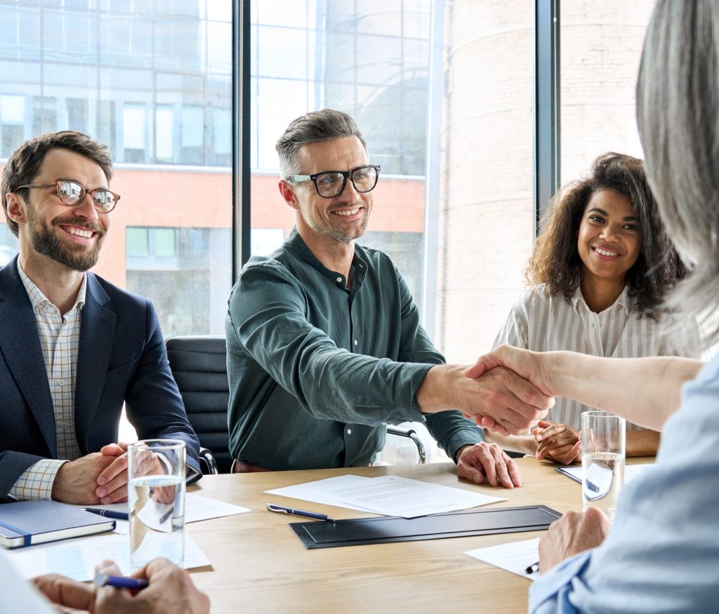 Happy,Businessman,And,Businesswoman,Shaking,Hands,At,Group,Board,Meeting.